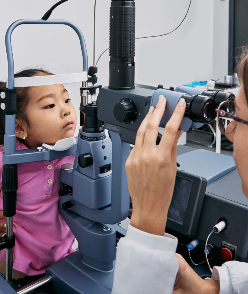 A young child wearing a pink shirt looks into optometry equipment during an eye examination.