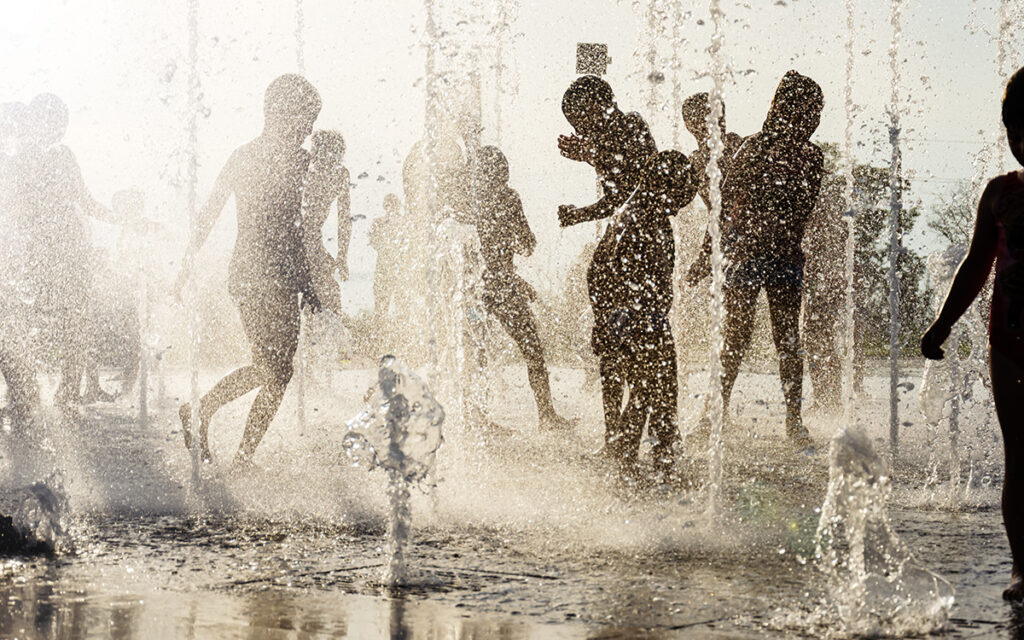 Silhouettes of joyful children playing in a water fountain on a hot summer day.