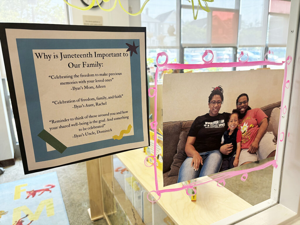 A window display consists of quotes on "Why is Juneteenth Important to Our Family" along with a photo of a young child seated between a woman and a man on a sofa. All three are smiling and have their arms around each other.