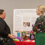 Two people have a conversation in front of a conference poster display about activities at the A. Sophie Rogers School for Early Learning.