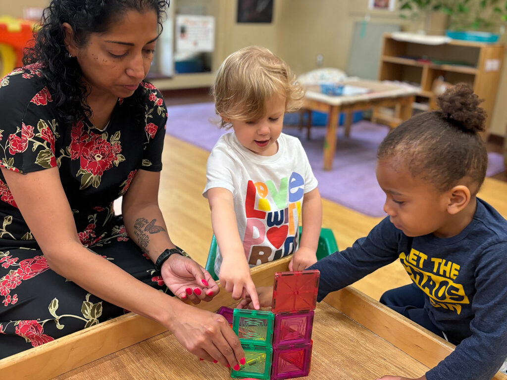 A teacher shows two small children several translucent, colored boxes.