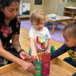 A teacher shows two small children several translucent, colored boxes.