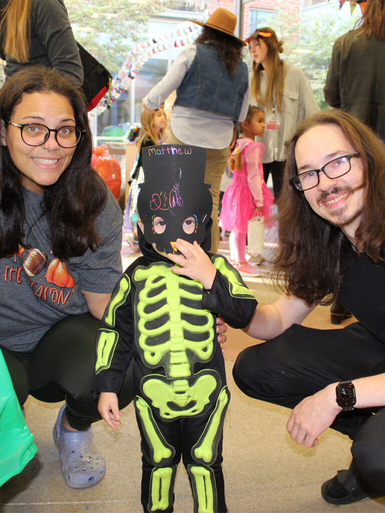 A woman and a man stand next to a small child dressed as a skeleton