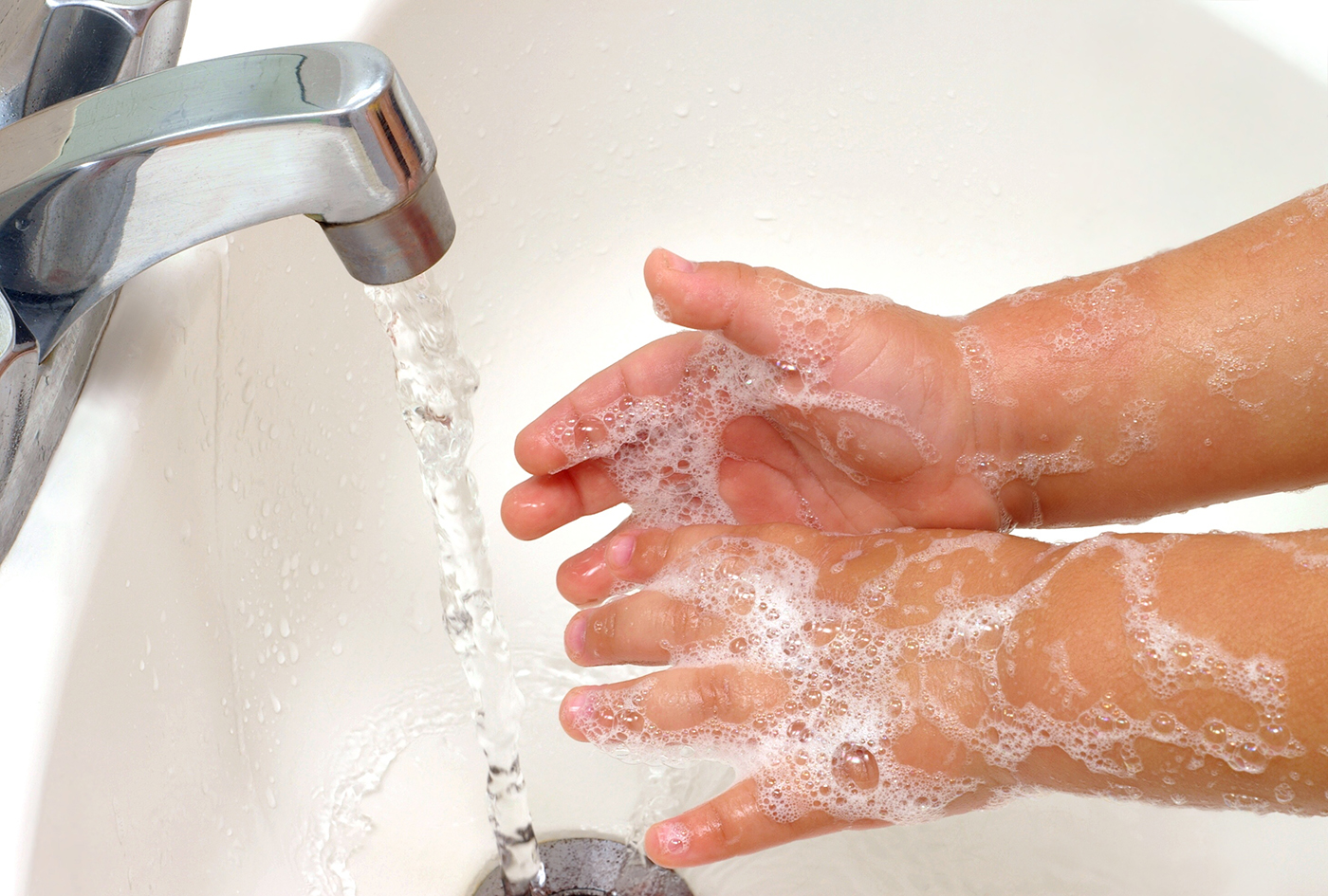 Closeup of a child's soapy hands being washed under running water in a sink